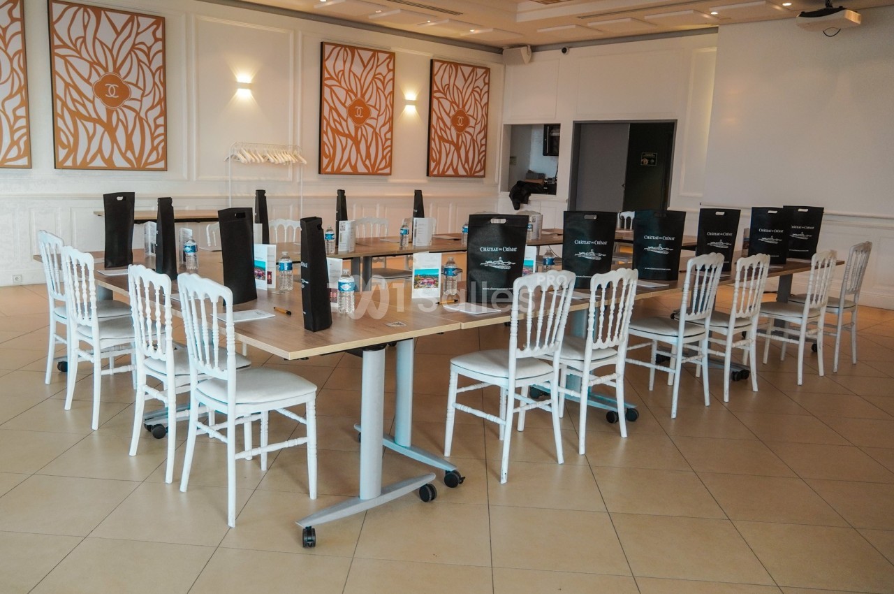 Salle de réunion aménagée avec des tables en bois, des chaises blanches, des sacs cadeaux et des bouteilles d'eau.