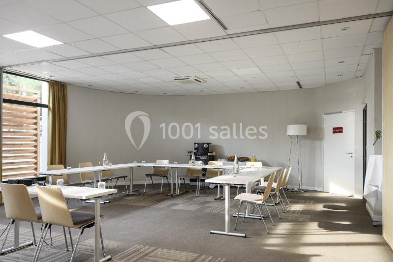 Salle de réunion lumineuse avec des tables disposées en U, chaises beige, et équipement de présentation.