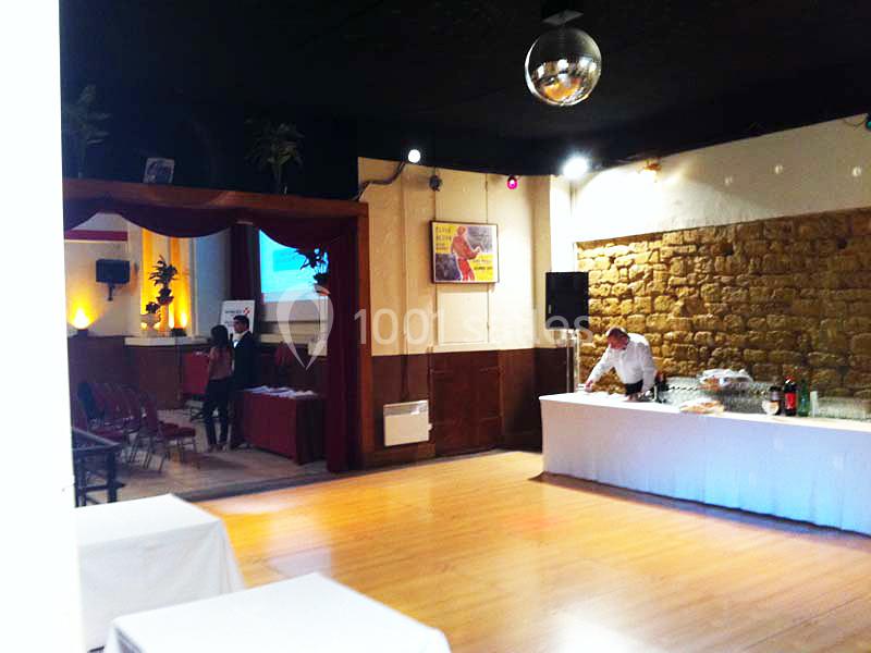 Salle avec parquet, tables dressées pour un buffet, écran de projection, et décorations murales en pierre et bois.