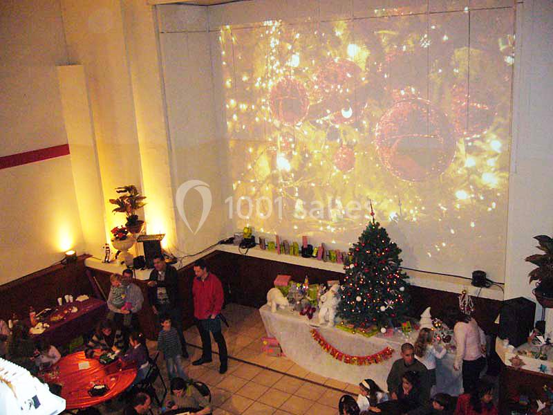 Salle décorée pour Noël avec un sapin illuminé, une table garnie et une projection murale d'ornements festifs.
