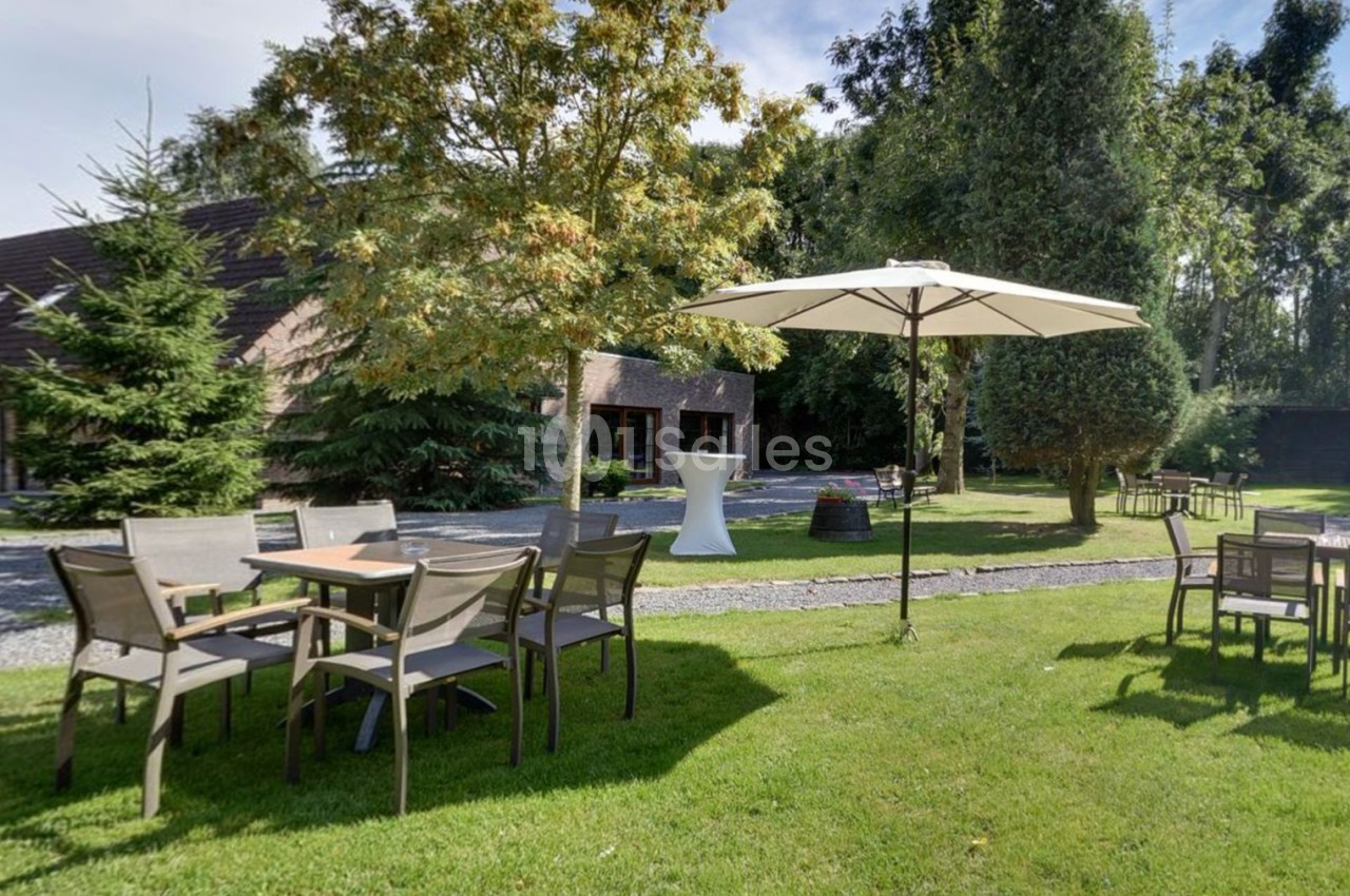 Tables et chaises en plein air sur une pelouse, avec un parasol et des arbres en arrière-plan.