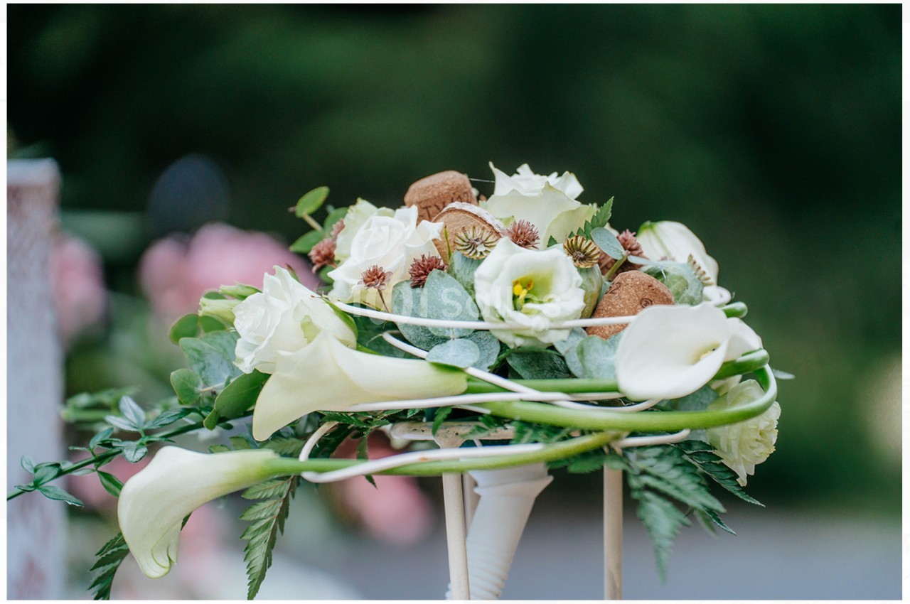 Composition florale avec des roses blanches, des callas et des feuillages verts, disposée sur un support décoratif.