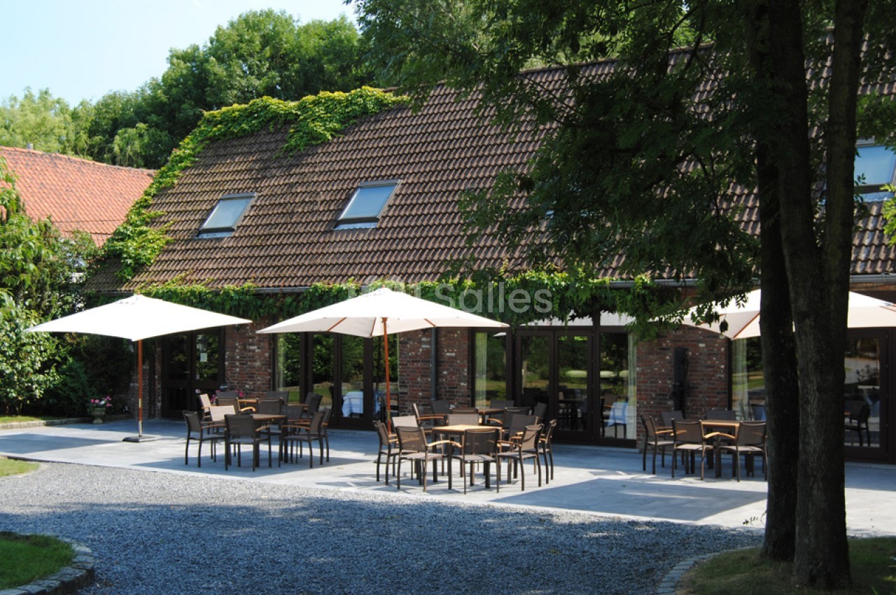 Terrasse extérieure avec tables, chaises et parasols devant un bâtiment en briques entouré de verdure.