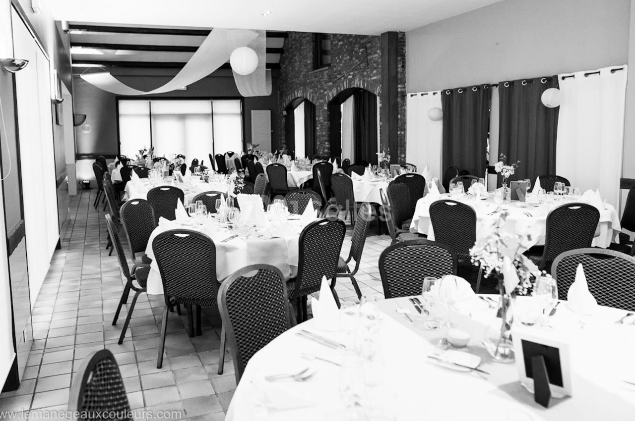 Salle de réception aménagée avec des tables rondes dressées, chaises noires et décoration sobre.