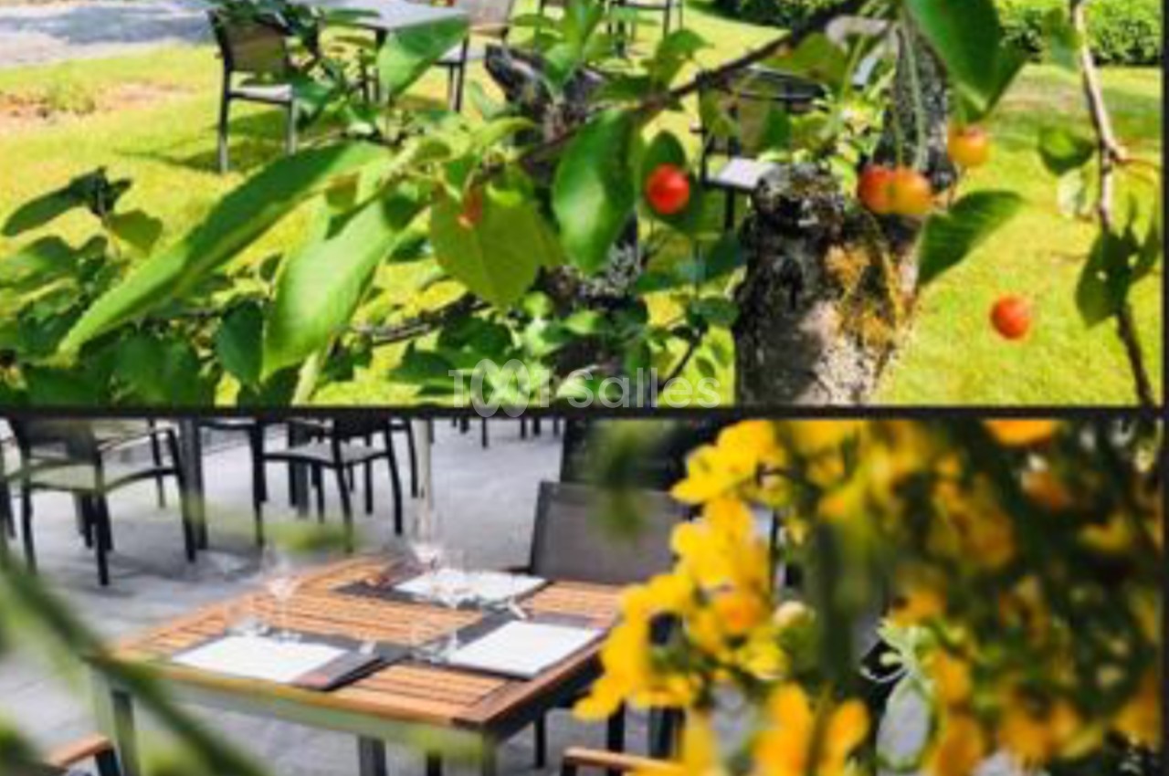 Des cerisiers en avant-plan et une terrasse extérieure avec tables dressées visibles en arrière-plan.