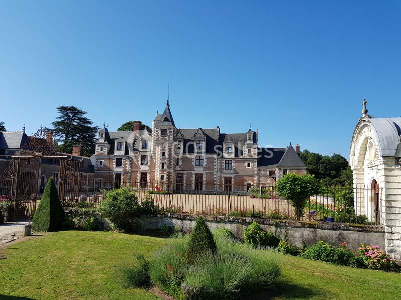 Façade d'un château en briques et pierres entouré de jardins verdoyants sous un ciel bleu clair.
