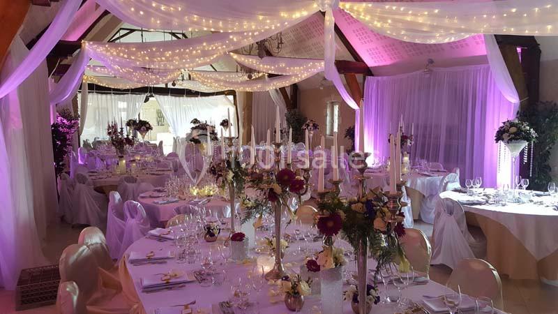Salle de réception décorée avec des guirlandes lumineuses, des tables dressées et des fleurs pour un événement festif.