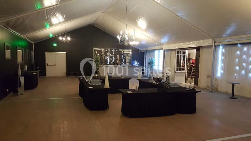 Intérieur d'une salle de réception sous tente avec tables noires dressées, bar éclairé et décor sobre.