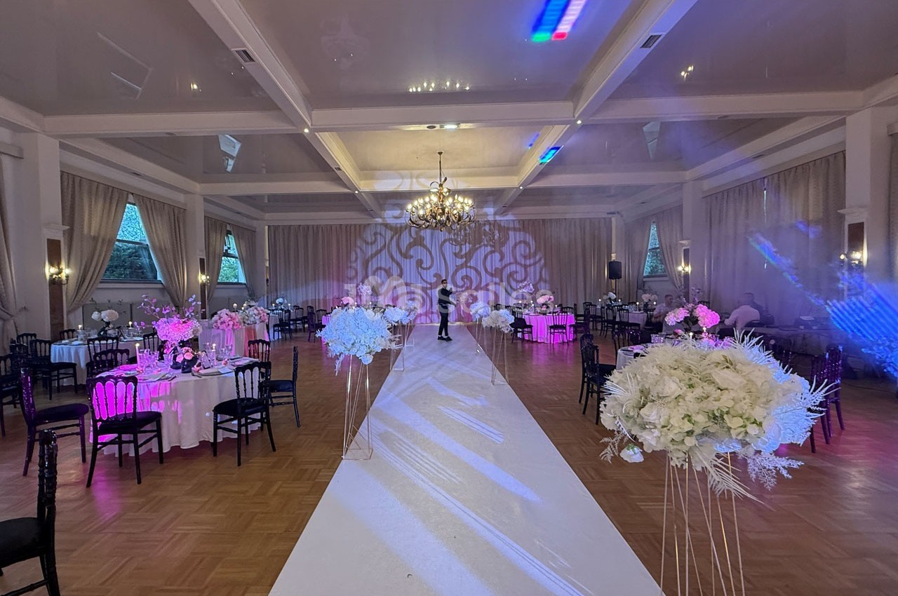 Salle de réception élégamment décorée avec des tables dressées, un tapis blanc central et des éclairages colorés.