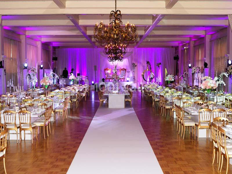 Salle de réception décorée avec des tables élégantes, des chaises dorées et un éclairage violet.