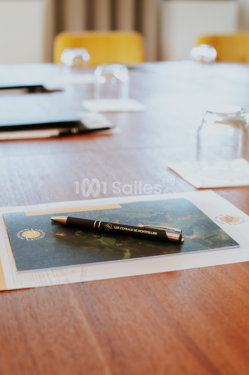 Stylo noir posé sur une carte sur une table en bois, entouré de verres et de dossiers.