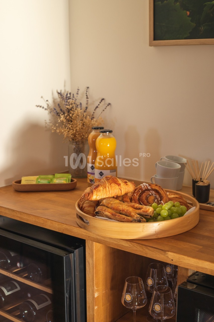 Plateau en bois avec viennoiseries, raisins et jus d'orange sur un buffet en bois, décoré de fleurs séchées.