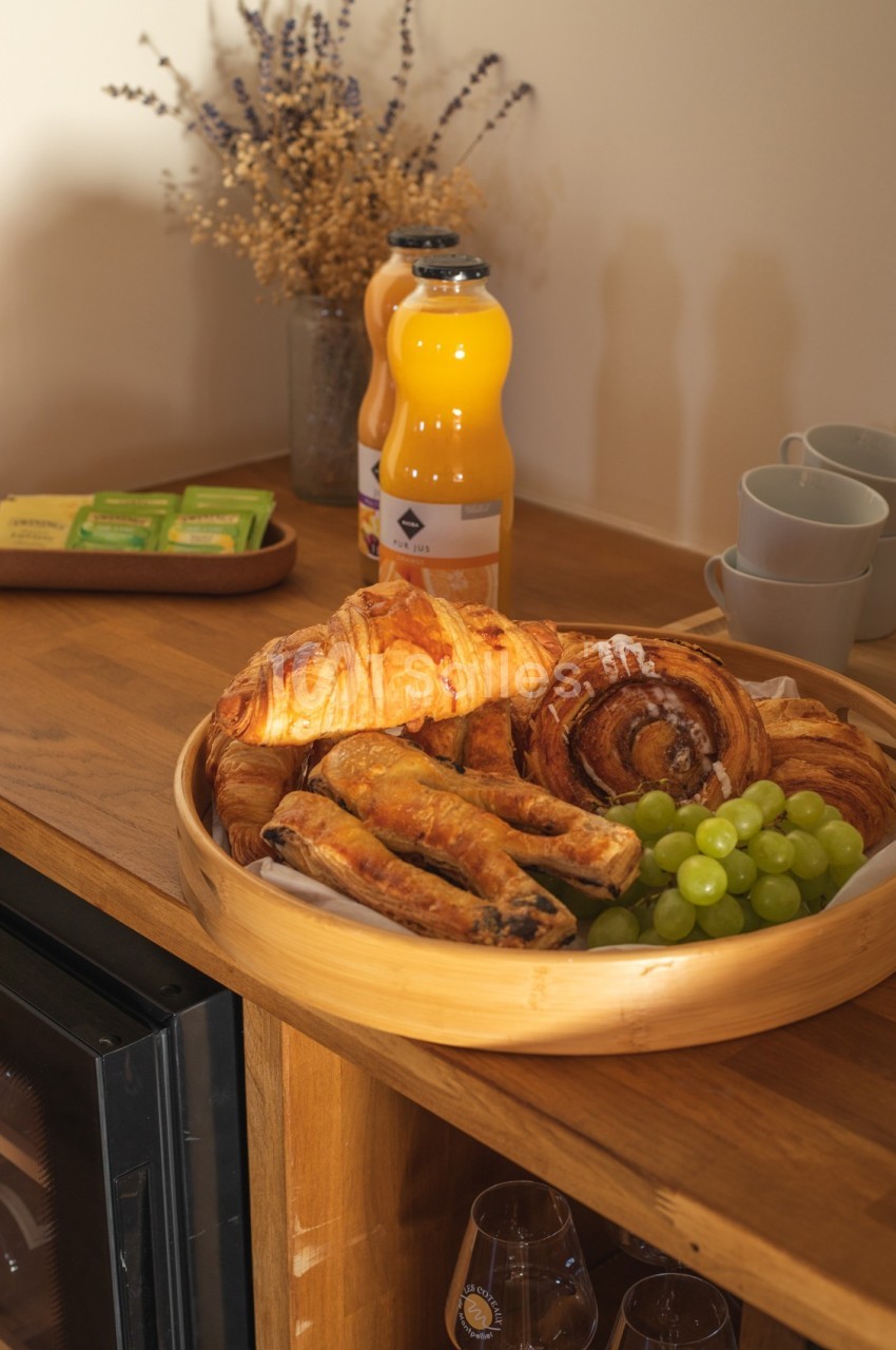 Plateau en bois avec croissants, pains au chocolat, raisin, jus d'orange et tasses sur un buffet en bois.