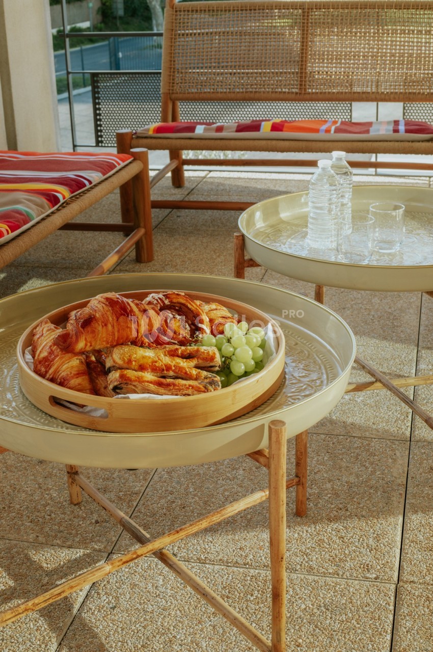 Plateau de viennoiseries et raisins posé sur une table basse en extérieur, avec des bouteilles d'eau et des verres à côté.