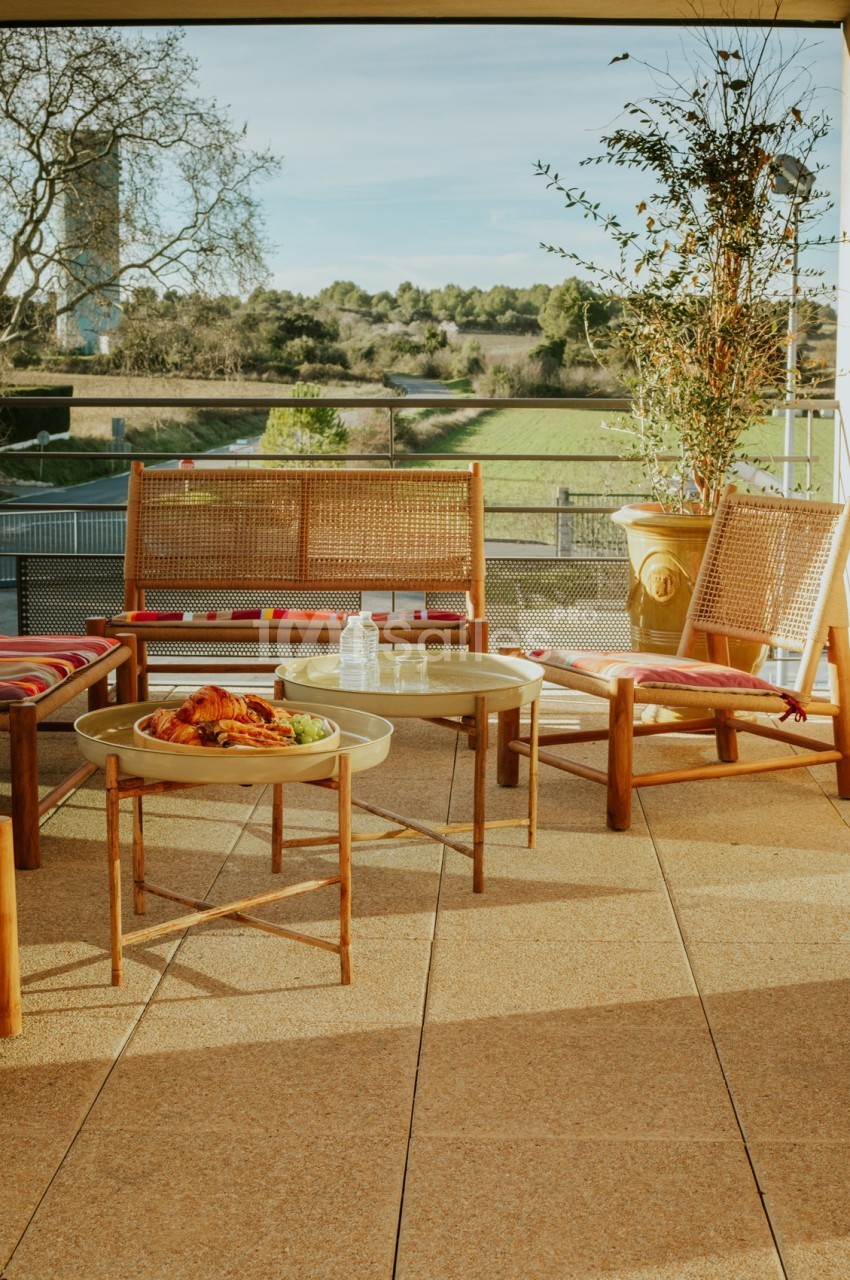 Mobilier de jardin en bois sur une terrasse ensoleillée avec vue sur un paysage verdoyant.