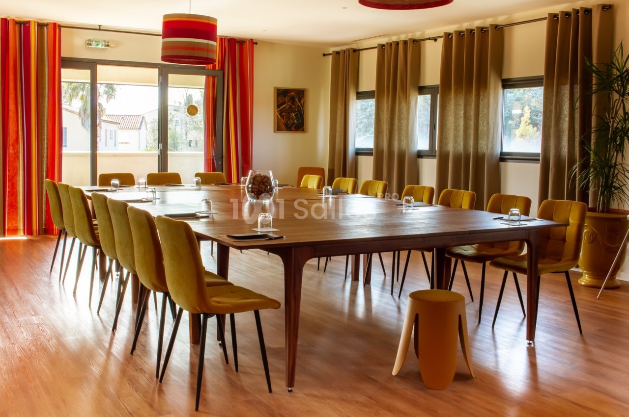 Salle de réunion lumineuse avec grande table en bois, chaises jaunes, rideaux colorés et grandes fenêtres.