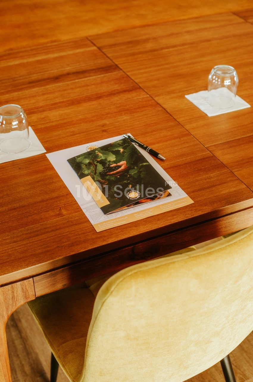 Document avec un stylo posé sur une table en bois, entouré de deux verres retournés et une chaise en tissu beige.