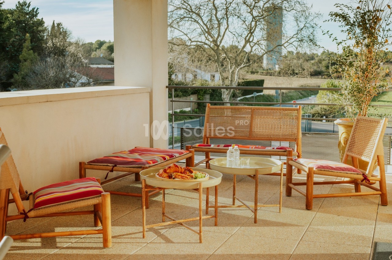 Mobilier en bois avec coussins rouges sur une terrasse ensoleillée, entourée de verdure et d'arbres.