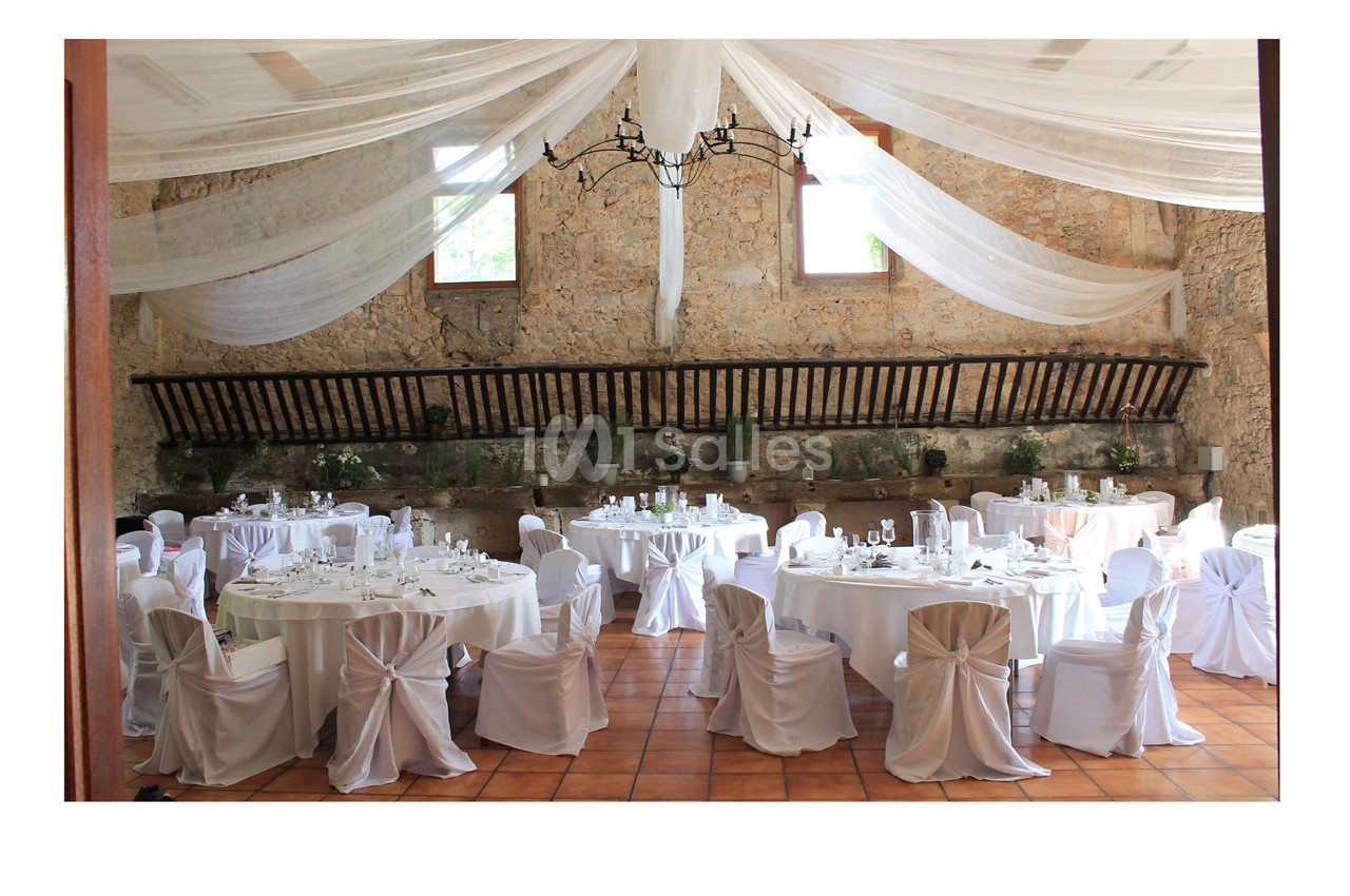 Salle de réception décorée avec des tables rondes nappées de blanc, des chaises assorties et un plafond drapé.