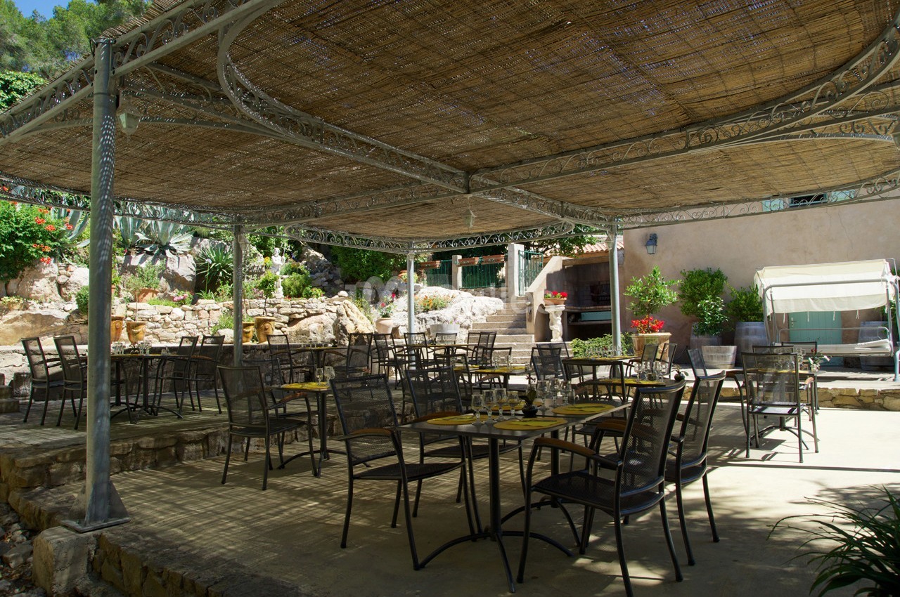 Terrasse ombragée avec tables et chaises en métal, entourée de végétation et de murs en pierre.