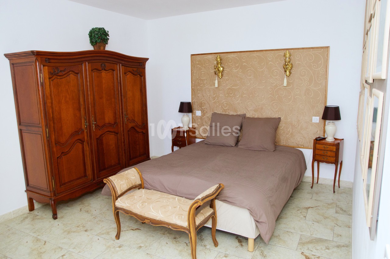 Chambre avec lit double, tête de lit décorative, armoire en bois, tables de chevet et banc assorti.