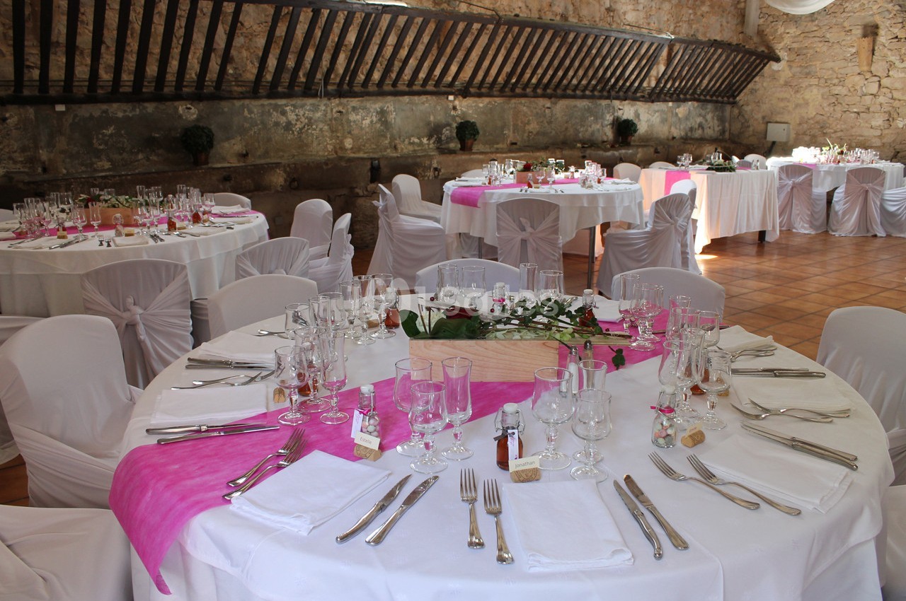 Salle de réception avec tables rondes décorées de nappes blanches et chemins de table roses, prête pour un événement.