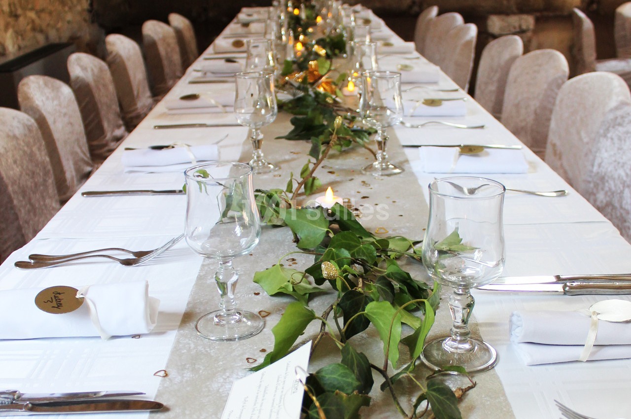 Table décorée pour un événement, ornée de feuillage, bougies et vaisselle élégante dans une ambiance chaleureuse.