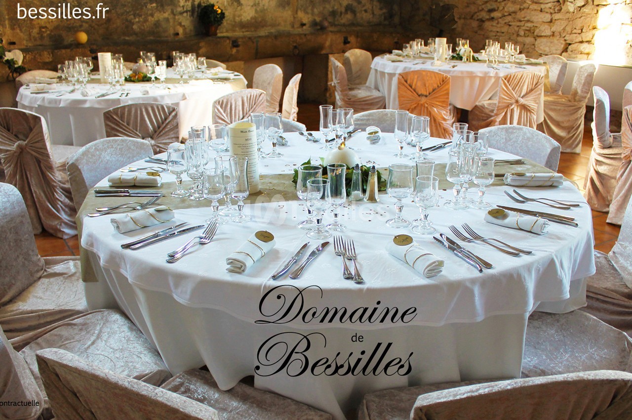 Tables rondes élégamment dressées avec nappes blanches, vaisselle raffinée et décorations dans une salle en pierre.