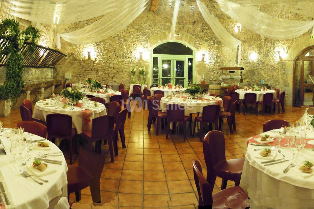 Salle de réception avec murs en pierre, tables rondes dressées et décorations élégantes sous un plafond drapé.