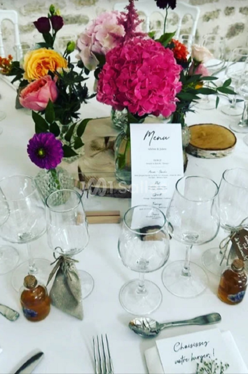 Table de réception décorée avec des fleurs colorées, des verres, des couverts, des menus et des petits cadeaux invités.