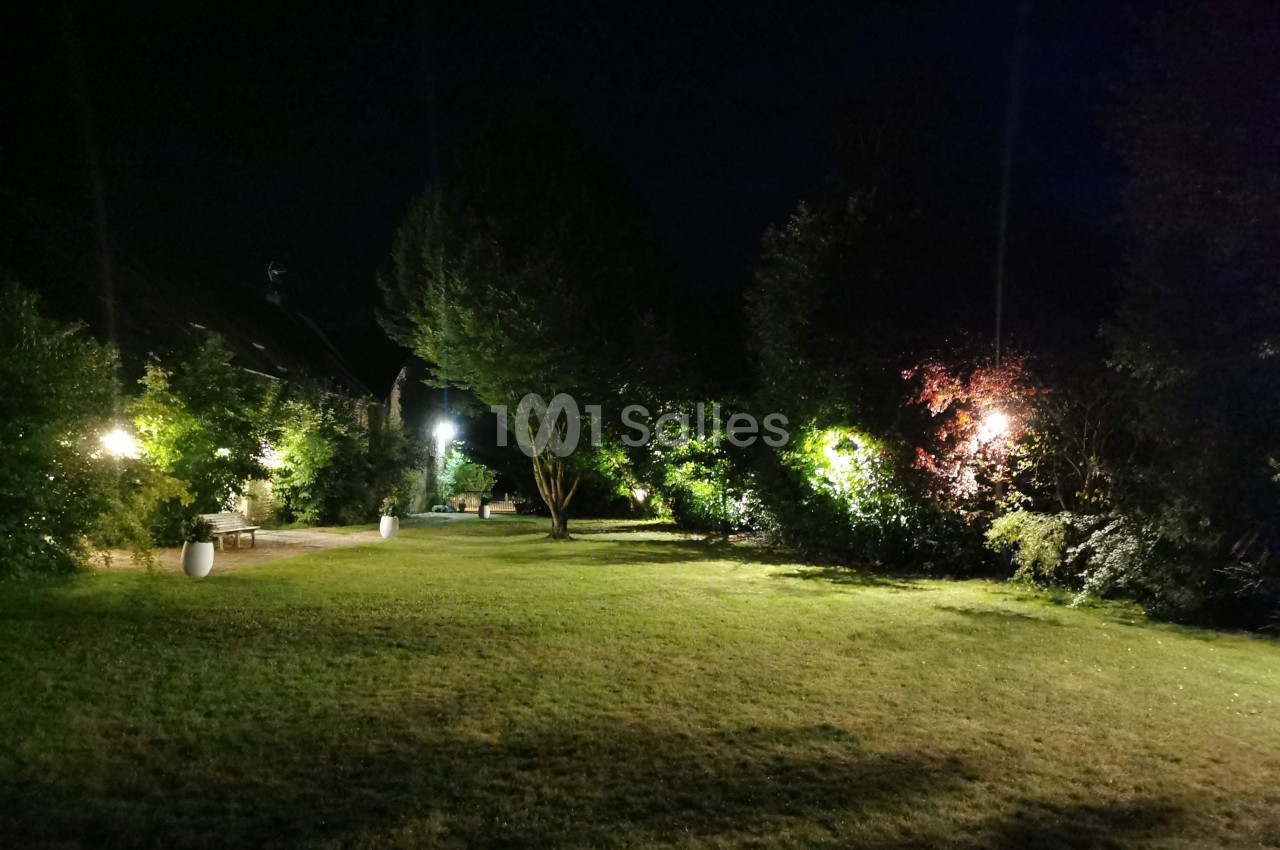 Pelouse éclairée la nuit avec des arbres et des buissons entourés de lumières tamisées.