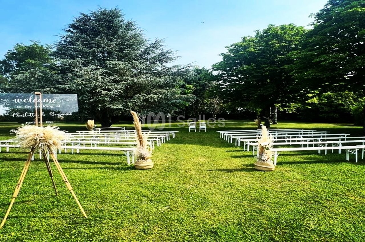 Chaises blanches alignées en extérieur sur une pelouse, entourées d'arbres, avec un panneau de bienvenue à gauche.
