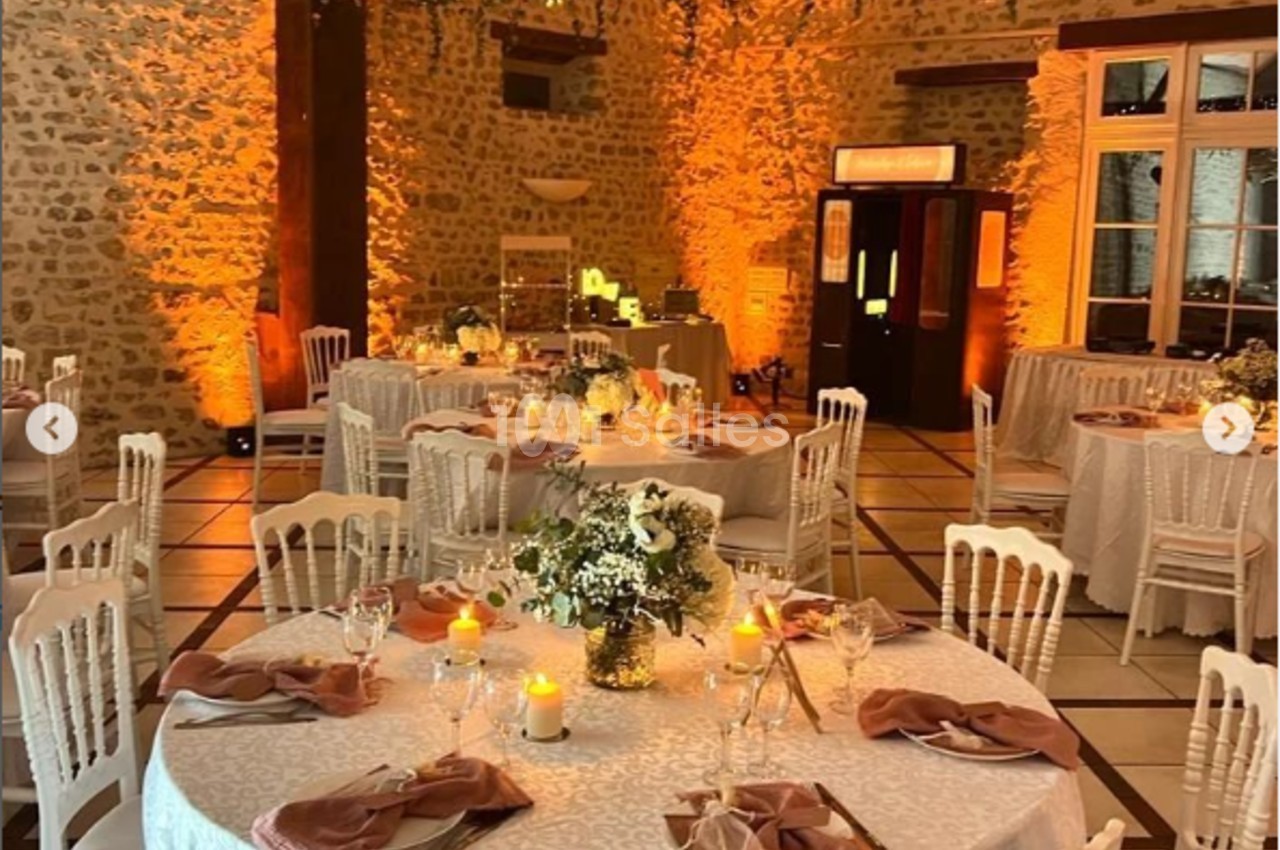 Salle de réception décorée avec des tables rondes, nappes blanches, bougies et guirlandes lumineuses suspendues.