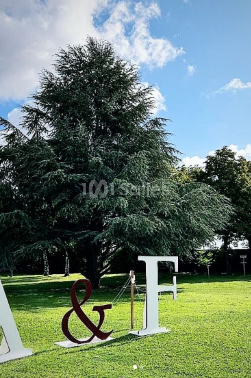 Lettres géantes ’A & F’ posées sur une pelouse verte, avec un grand arbre et un ciel bleu en arrière-plan.