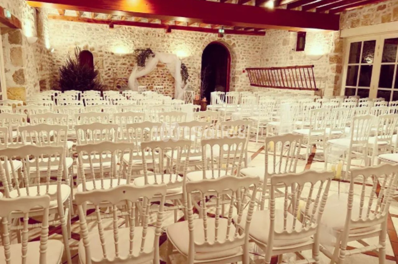 Salle de réception en pierre avec des chaises blanches alignées et une décoration légère en arrière-plan.
