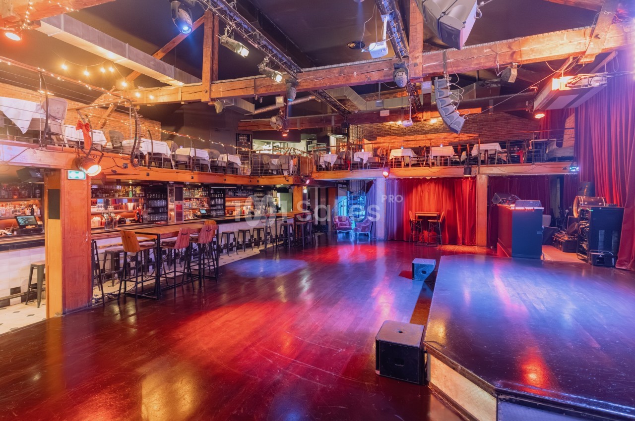 Salle de spectacle avec scène, piste de danse, bar et mezzanine aménagée avec tables et chaises.