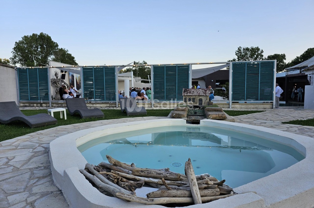 Petit bassin rond entouré de pierres, avec des transats et des panneaux en bois devant un espace extérieur animé.