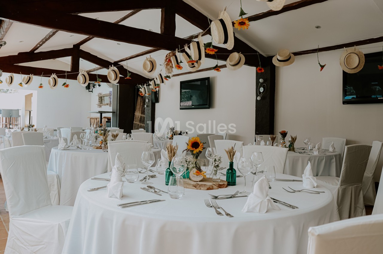 Salle de réception décorée avec des tables rondes dressées, des chapeaux suspendus et des touches de tournesols.