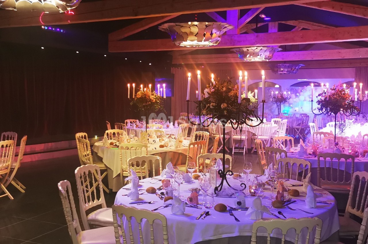 Salle de réception décorée avec des tables rondes, chandeliers et éclairage tamisé pour un événement festif.