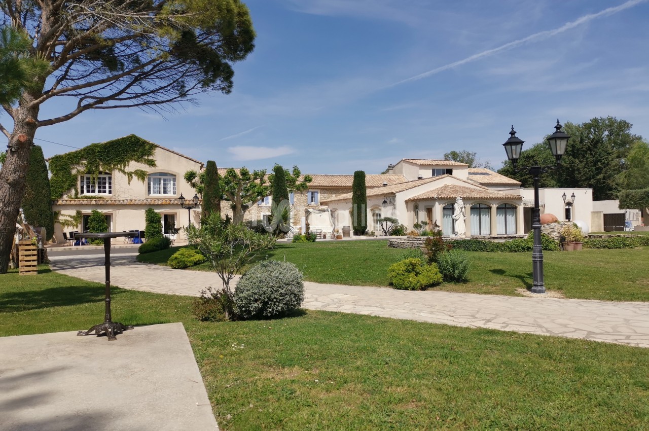 Bâtiments de style provençal entourés de verdure, avec un chemin pavé et des lampadaires au premier plan.