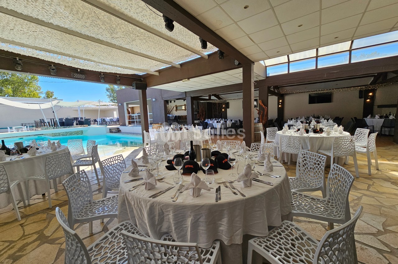 Salle de réception avec tables rondes dressées, chaises blanches et vue sur une piscine extérieure.