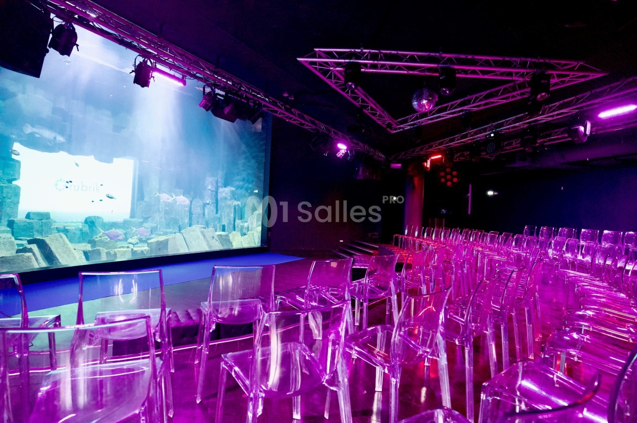 Salle de conférence avec des chaises transparentes et un écran géant affichant une scène sous-marine.