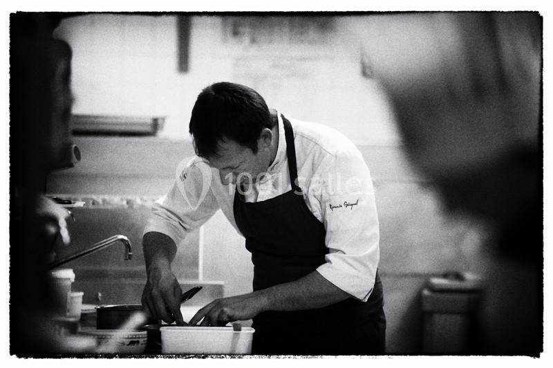 Un chef en tablier prépare un plat dans une cuisine professionnelle, concentré sur son travail.