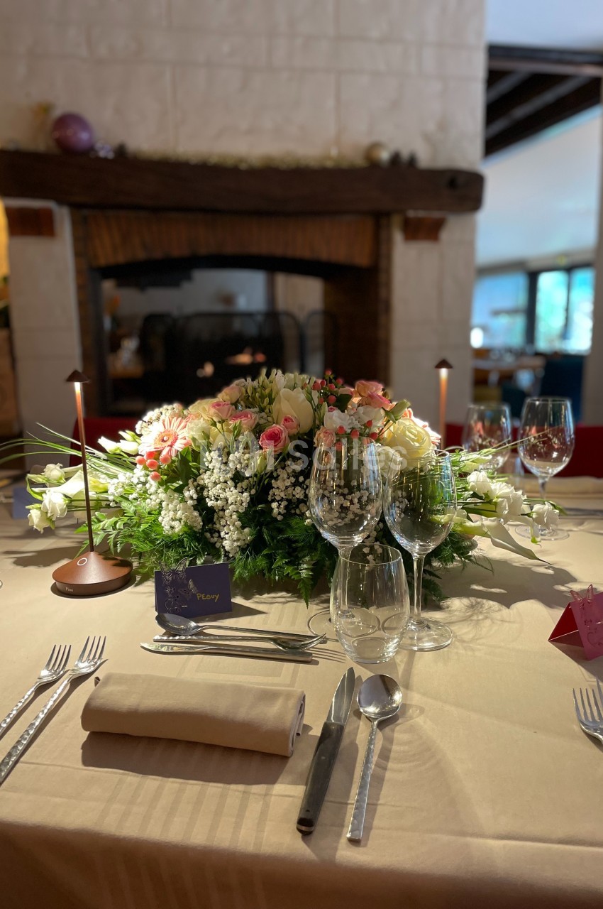 Table élégamment dressée avec un centre de table floral, des verres à vin et des couverts, devant une cheminée.