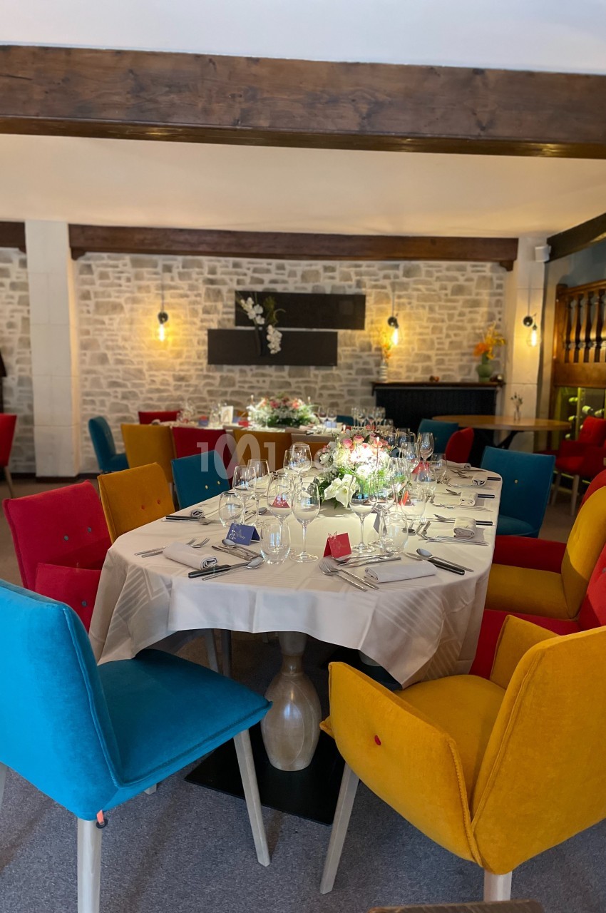 Salle de restaurant avec tables dressées, chaises colorées et murs en pierre apparente éclairés par des appliques.