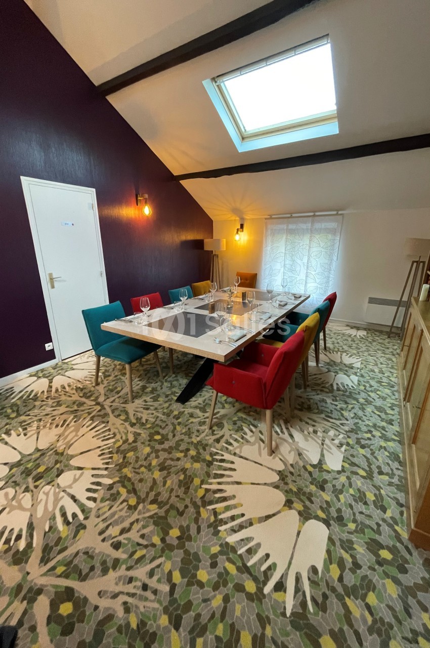 Salle à manger lumineuse avec table dressée, chaises colorées, tapis à motifs et fenêtre de toit.