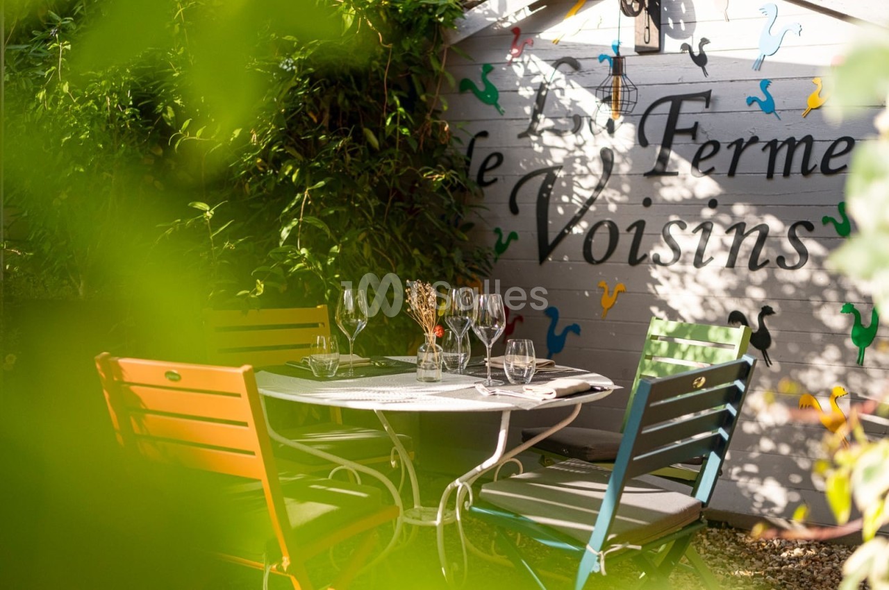 Table de jardin entourée de chaises colorées, disposée dans un coin verdoyant près d'un mur décoré.