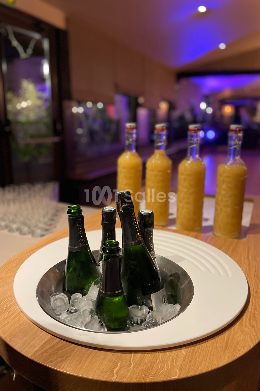 Bouteilles de champagne sur glace et carafes de jus disposées sur une table dans un espace éclairé.
