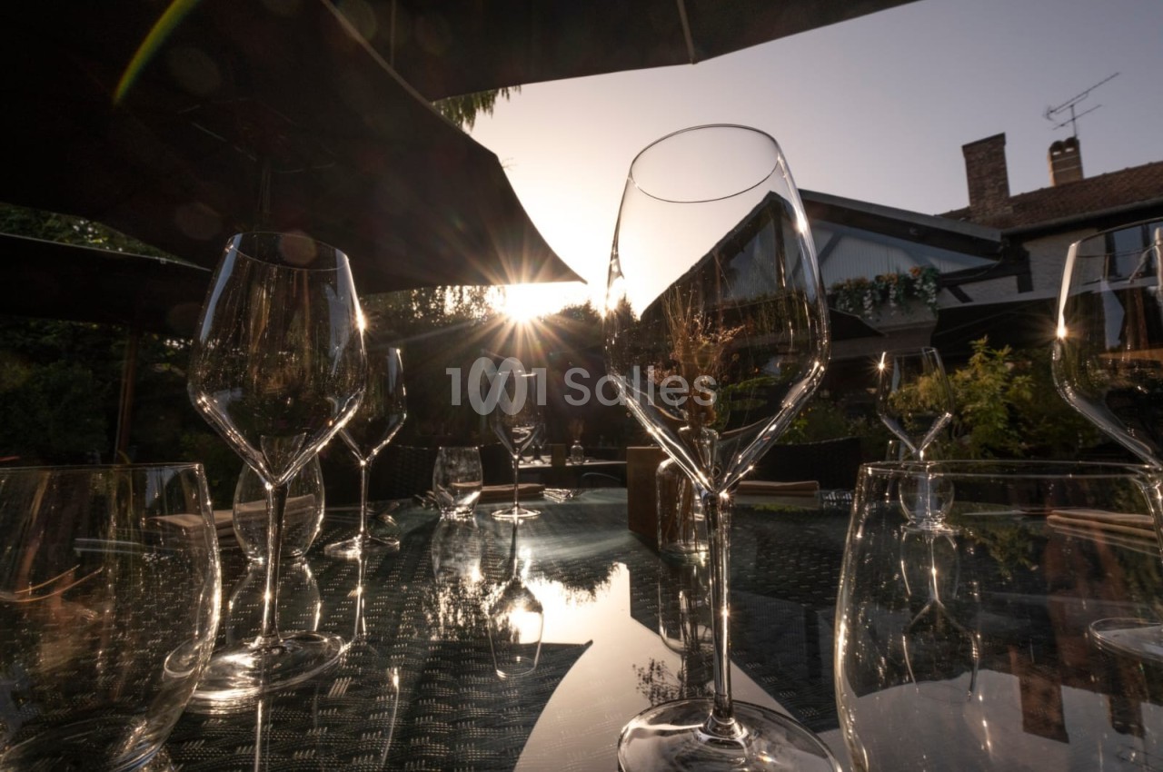 Verres à vin vides sur une table en extérieur, éclairés par le soleil couchant avec des parasols et des bâtiments en arrière…