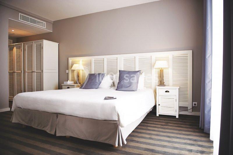 Chambre lumineuse avec un grand lit, deux tables de chevet, lampes allumées et armoire blanche dans un décor épuré.